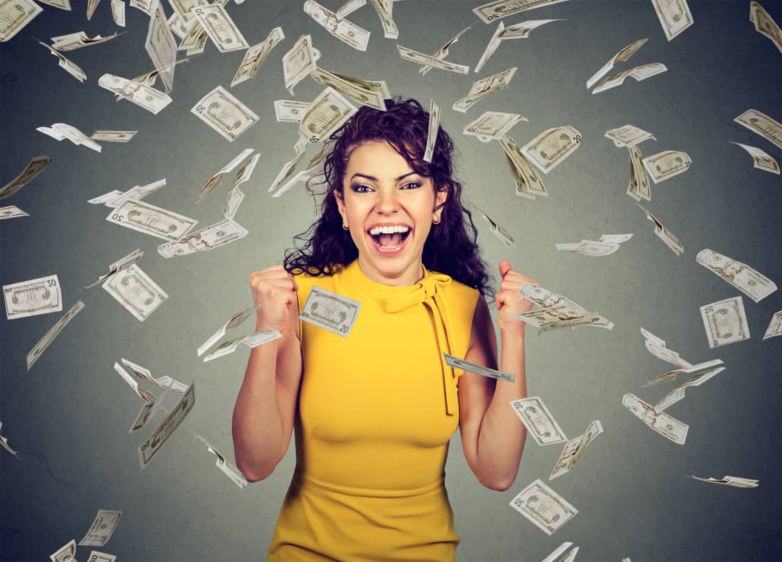 Portrait happy woman pumping fists ecstatic celebrates success under a money rain falling down dollar bills banknotes isolated on gray wall background with copy space