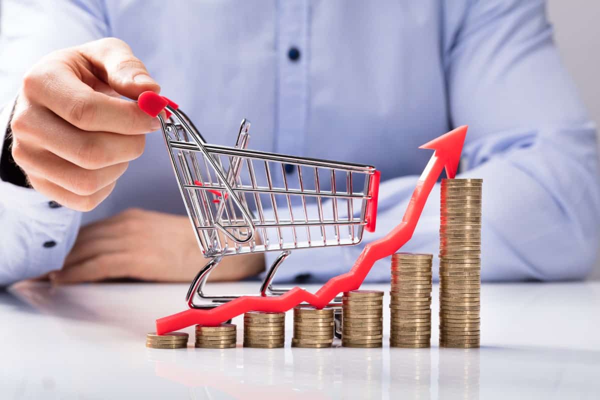 Increasing Graph Of Coins In Front Of Human Hand Holding Small Shopping Cart