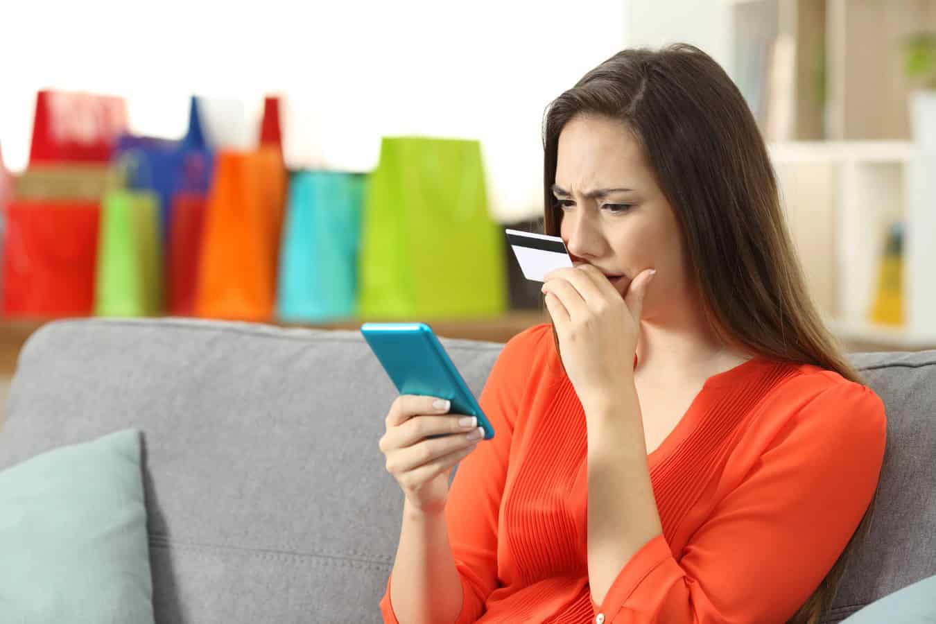 Worried lady buying online with credit card and phone sitting on a couch