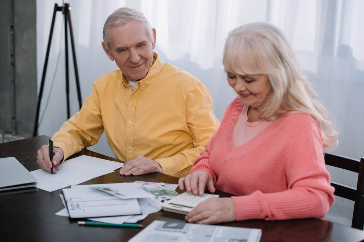 Happy Senior coupe sitting at table with calculator and counting money