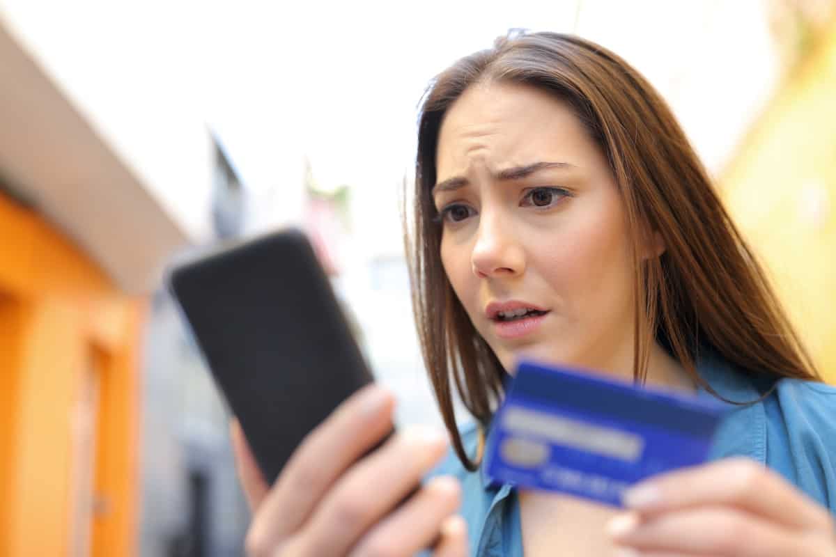 Worried woman pays online with credit card and smart phone in the street