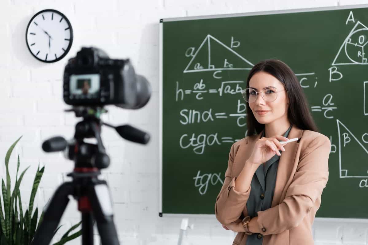 Online Tutor Woman holding chalk near blurred digital camera and chalkboard