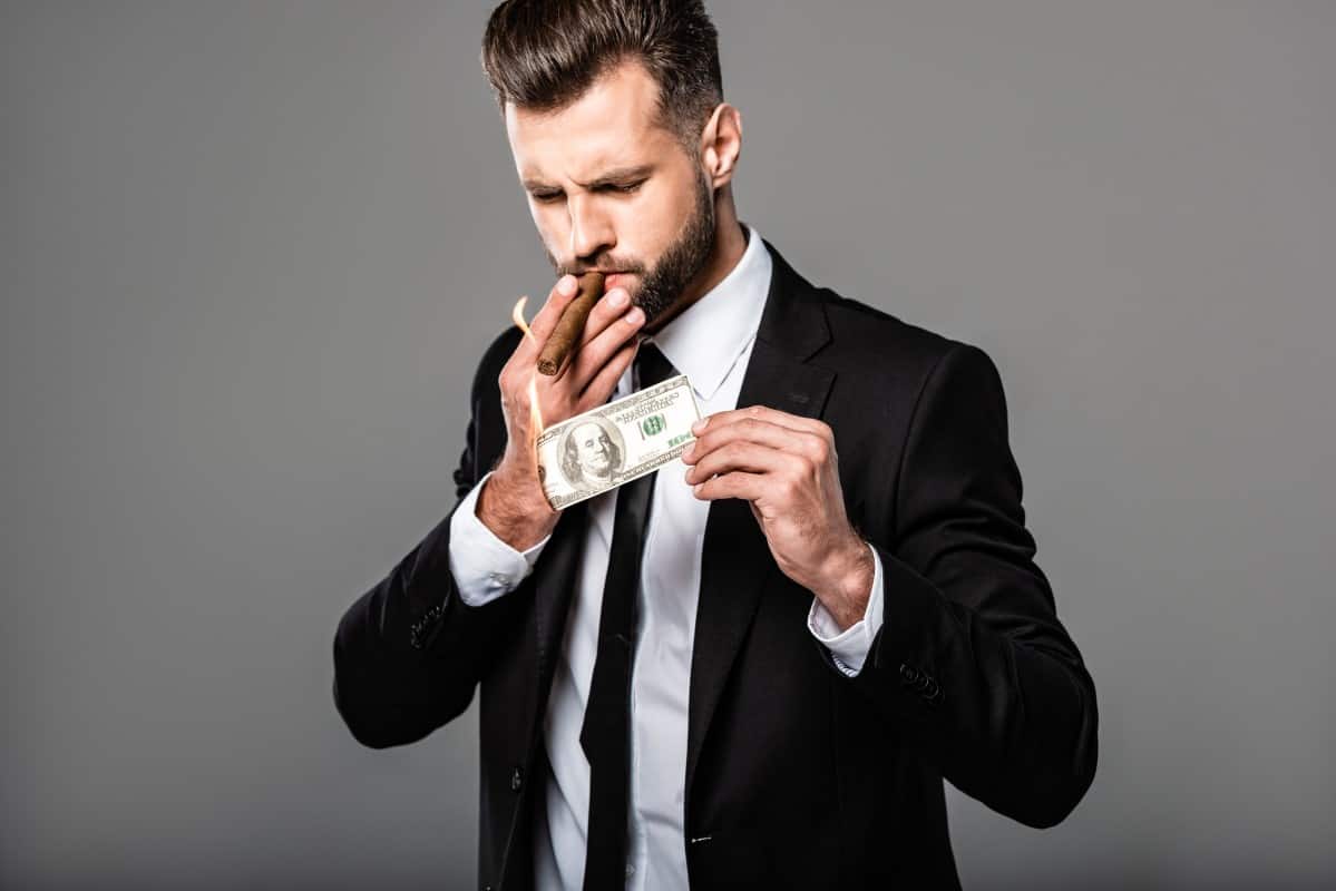 Rich successful businessman in black suit lighting up cigar from burning money Evil Investor 