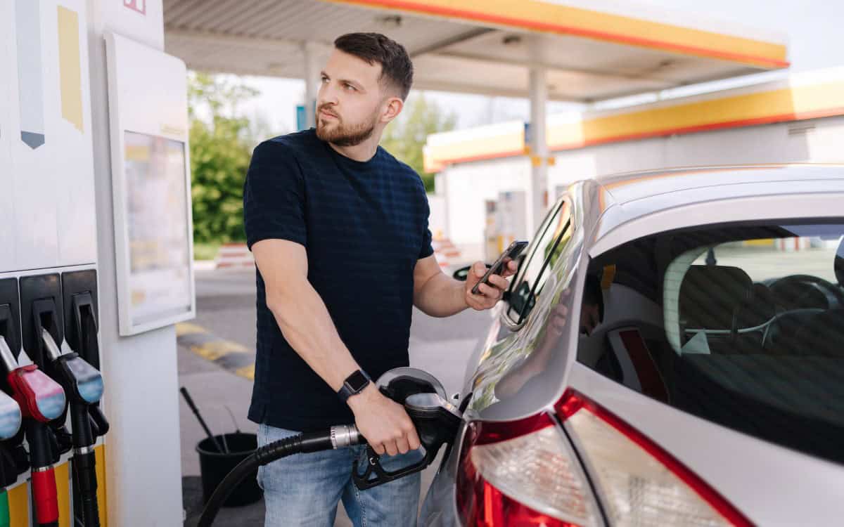 Handsome bearded man refueling car and looking on the scoreboard while standing on self service gas station. High quality photo