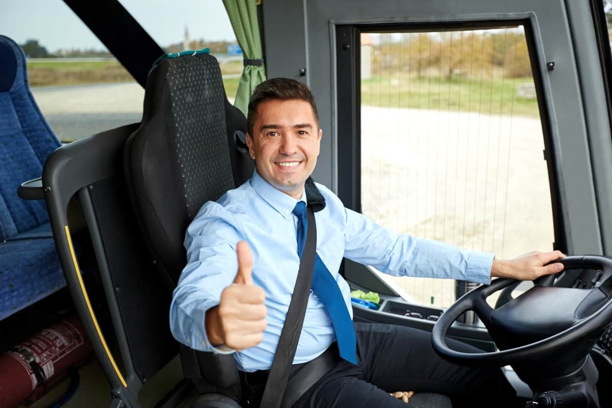 transport, tourism, road trip and people concept - happy bus driver driving intercity bus and snowing thumbs up