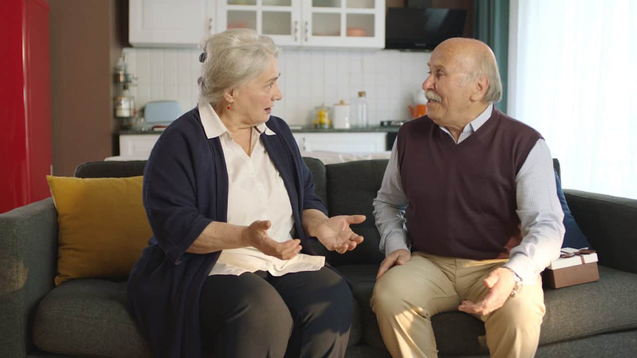 An elderly couple sitting in their armchair at home and arguing