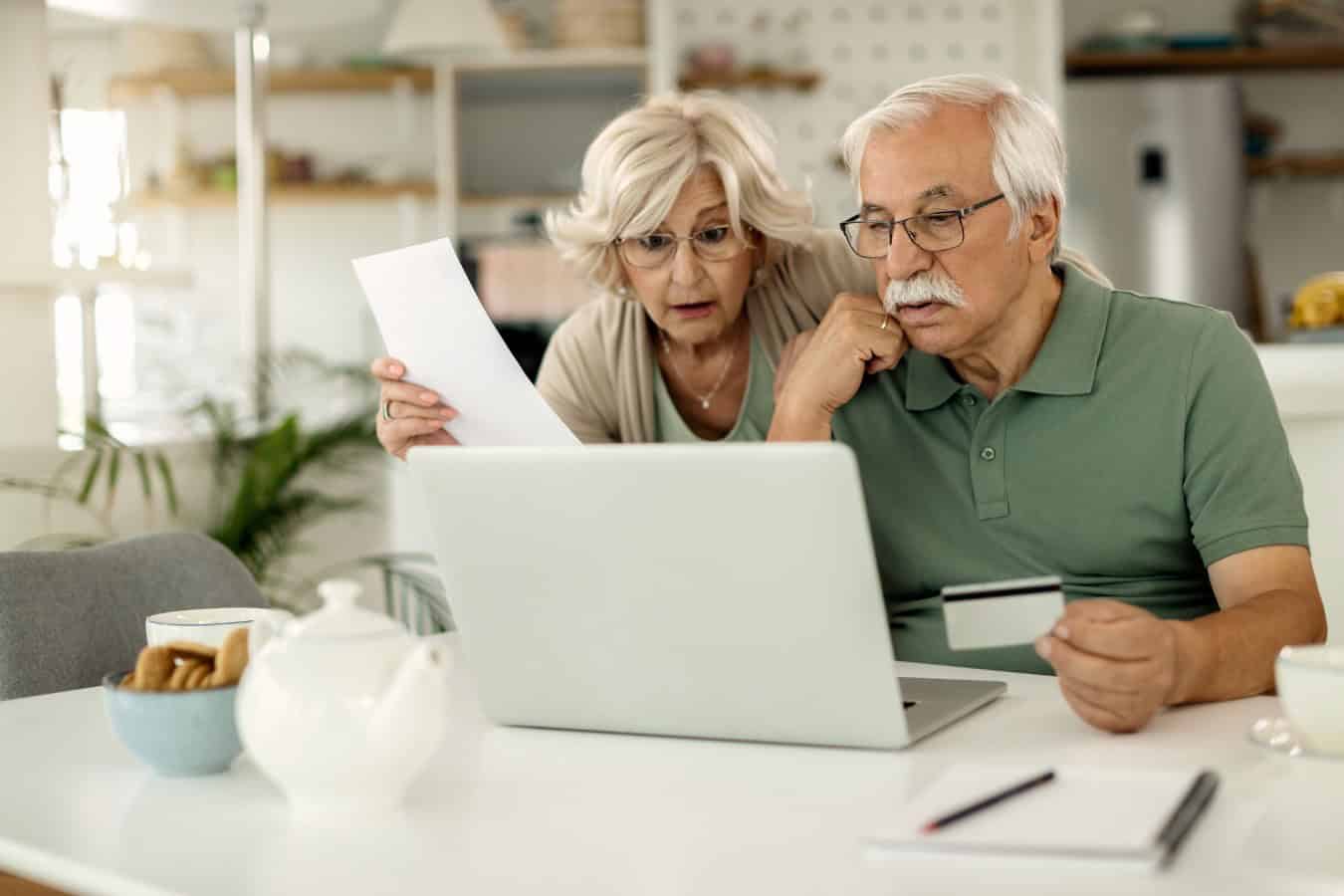 Worried mature couple using laptop and credit card while checking their online bank account and analyzing their finances at home.