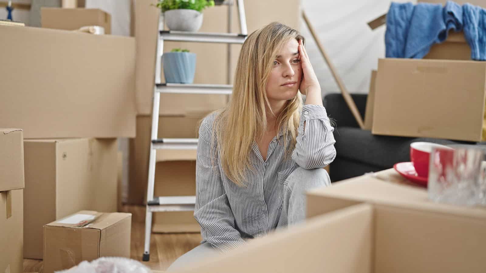 Young woman sitting on floor with stressed expression at new home