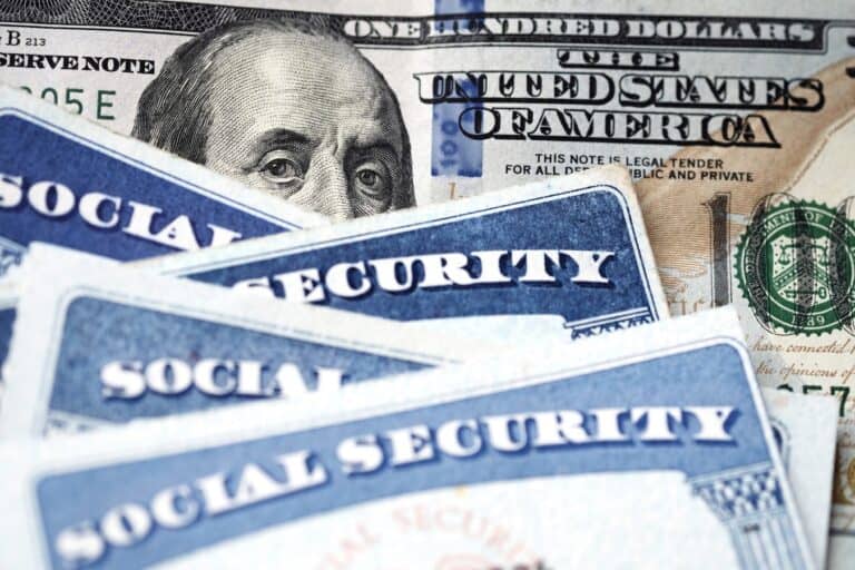 Several Social Security Cards on a US United States one hundred dollar bill $100 system of benefits for retired elderly people