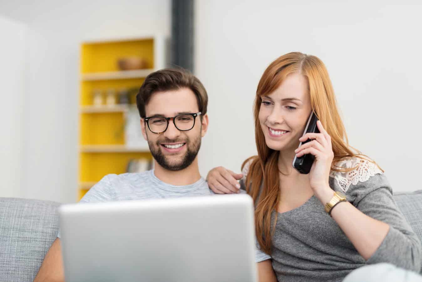 Couple with Laptop and Telephone Sitting on Sofa