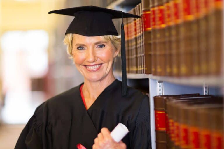 Older graduate student standing near bookshelf