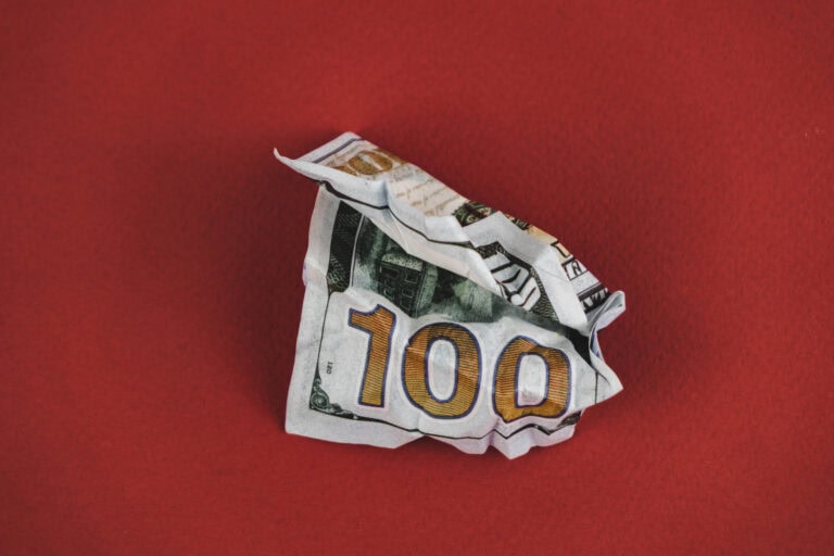 crumpled hundred dollar bill lying on a red background.