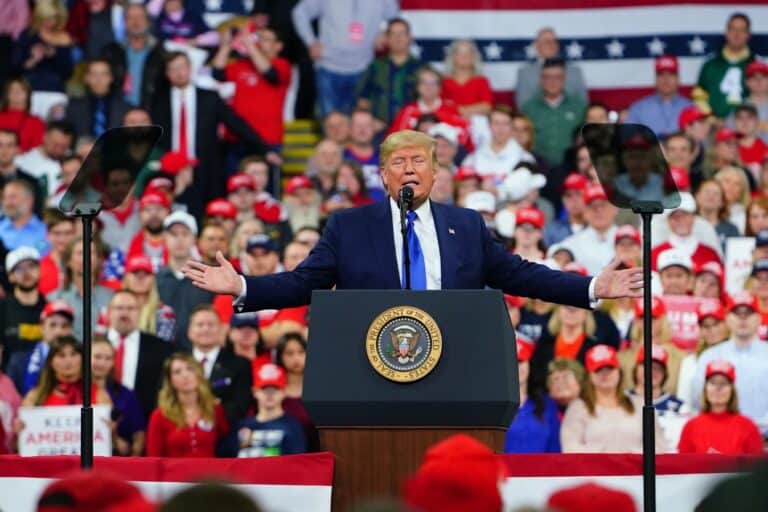 Donald Trump speaking at a rally with supporters in the background.